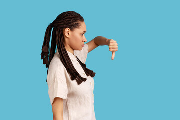 Side view of discontent woman with black dreadlocks showing disapproval sign, keeps thumb down,...