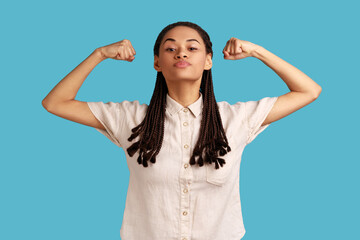 Yes, I am winner. Confident woman with black dreadlocks raises arms, demonstrates muscles, being...