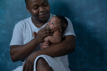 Happy African father holding 4 mouth newborn baby in his arms, sitting and leaning on blue...