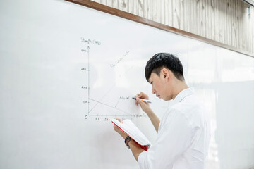 Naklejka na ściany i meble An Asian male teacher in a classroom near the whiteboard is writing and teaching a lesson with a special lecture in a class column. Math teacher explains arithmetic sums to university students