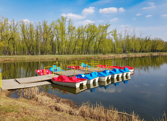 Colorful catamarans stand in a row at the wooden pier. Calm surface of the lake for water...