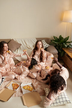 Group of young women in pajamas eating pizza and enjoying sleepover in friends house