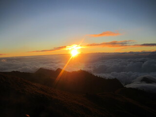 Sunrise at the top of Mount Rinjani in Lombok Island, Indonesia. View of crater lake covered in clouds from the summit. Beautiful sun rising in the horizon.