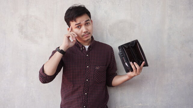 Young asian man with hands on head expression holding empty wallet