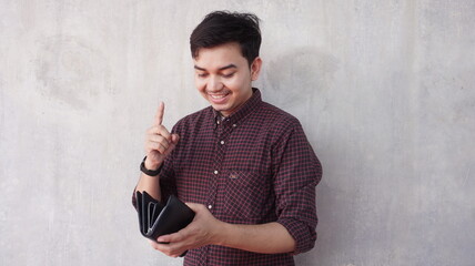 Young asian man in shirt smiling while holding wallet in hand