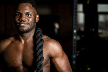 Muscular african american man posing with rope in gym. 