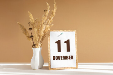 november 11. 11th day of month, calendar date.White vase with dried flowers on desktop in rays of...