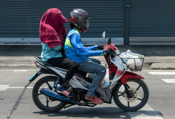  A motorcycle taxi rides on the street with a woman hidden under a towel
