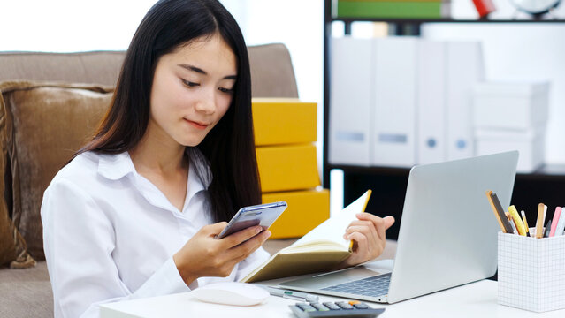 Work from home, Asian woman using mobile phone while working with laptop computer at home office, Asia female using smartphone at home office, Happy girl learning by internet, study online education