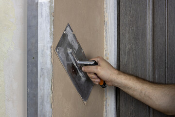 A worker applies plaster to a wall with a spatula.