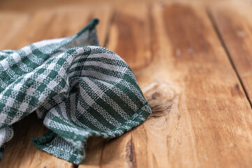 A green checkered kitchen towel lies on the countertop of a wooden table. Crumpled Towel or kitchen napkin on rough boards. Selective Focus.