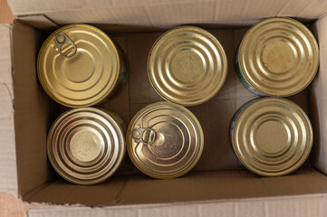 Canned food in a cardboard box. Tin cans with food ready to eat. Selective focus.