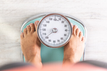 Woman looks down at the number of pounds or kilograms as she stands on a weighing scale