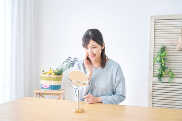 リビングで笑顔で卓上ミラーを見る女性