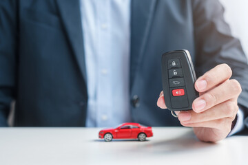 Businessman hand holding remote keyless with car toy, pen and contract document. buy and sale, insurance, rental and contract agreement concepts