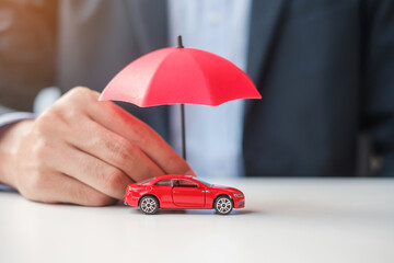 Businessman hand holding umbrella and cover  red car toy on table. Car insurance, warranty, repair,...