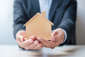 Businessman hand holding wooden Home model. Real estate, buy and sale, Property insurance, rental and contract agreement concepts