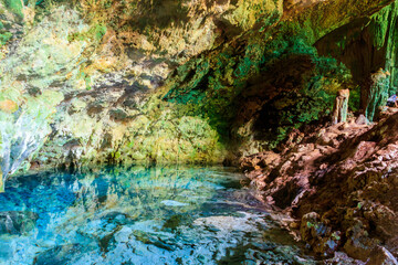 View of beautiful natural pool of crystal clear water formed in a rocky cave with stalagmites and...