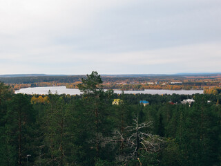 Fototapeta na wymiar Forest and river landscape from a hill with rooftops in Rovaniemi, Finland.