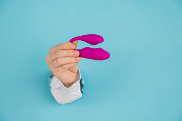 A woman's hand holds a pink sex toy through a hole in a paper blue background.