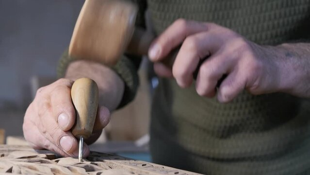 male hands of a wood carving master holding a wooden hammer and a sharp awl with a wooden handle tapping a pattern on a wooden board. Hobby and craft
