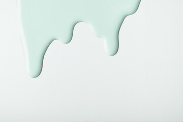Light cyan liquid drops of paint color flow down on isolated white background. Abstract green backdrop