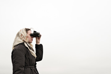 A woman is holding vintage binoculars and looking up at the gray sky.