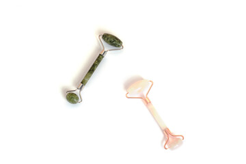Two cosmetic facial rollers, rose quartz crystal and jade isolated on white background, top view