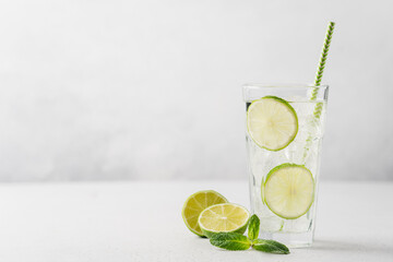 Lime mojito or lemonade with ice in tall glass  with straw on light gray background with copy space. Summer refreshing drink - obrazy, fototapety, plakaty