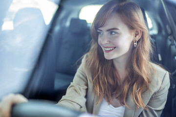 Fototapeta na wymiar Beautiful smiling young redhead woman behind steering wheel driving car.