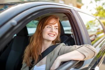 Fototapeta na wymiar Beautiful young woman driving her new car at sunset. Woman in car. Close up portrait of pleasant looking female with glad positive expression, woman in casual wear driving a car