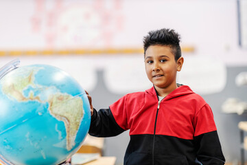 A smart Indian boy with globe on geography class.