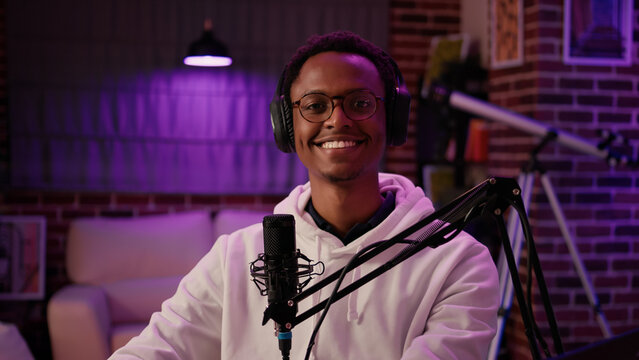 Portrait of man content creator smiling confident at camera while answering questions from listeners in home recording studio. African american online radio host reading fan mail from laptop computer.