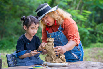 Asian little girl and teacher working with pottery clay together, happy kid creating handmade...
