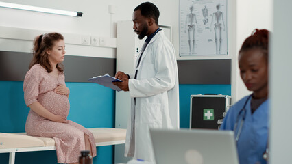 General practitioner doing pregnancy consultation with future mother, helping with childbirth. Health specialist talking to woman expecting child in medical office, checkup visit.