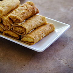 Delicate pancakes with cottage cheese on a white square plate on a dark background.