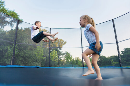 A boy and a girl jump on a trampoline without parental supervision. Brother and sister play on the trampoline in the park in summer
