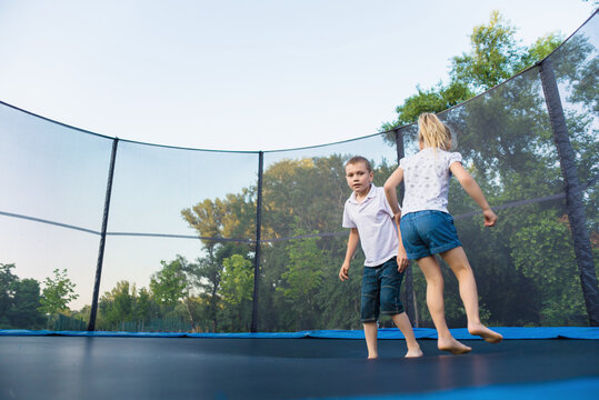 A boy and a girl jump on a trampoline without parental supervision. Brother and sister play on the trampoline in the park in summer