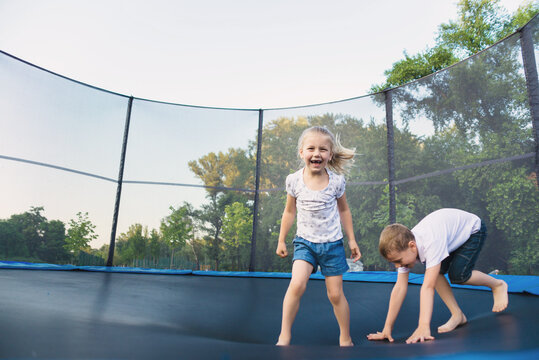 A boy and a girl jump on a trampoline without parental supervision. Brother and sister play on the trampoline in the park in summer