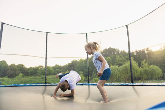 A boy and a girl jump on a trampoline without parental supervision. Brother and sister play on the trampoline in the park in summer