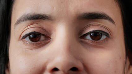 Macro shot portrait of authentic indian woman blinking in front of camera, having big brown eyes...