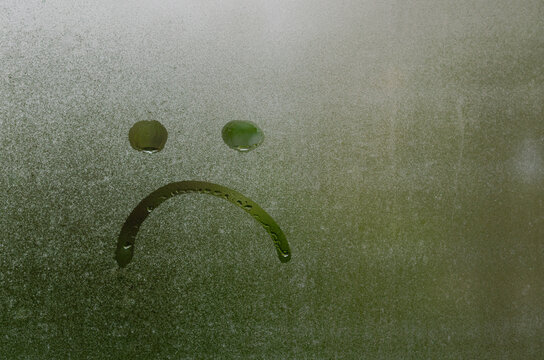 Face expession as boring and sad painted on window which fogged up after rain with blurred green color background.