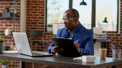 Project manager analyzing statistics plan with application report on laptop at office desk. Company...