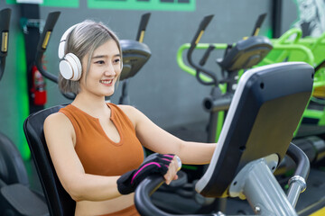 Fototapeta premium Young woman with headphone riding on a bicycle- gym fitness. Concept of healthy lifestyle.