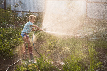 Slow life. Enjoying the little things. Summer holiday. Happy kid playing with garden hose and...