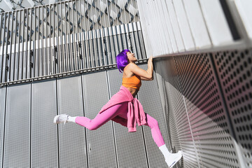 Happy woman wearing colorful sportswear climbing on the wall