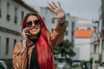happy red-haired woman talking on the phone and waving hand on the street