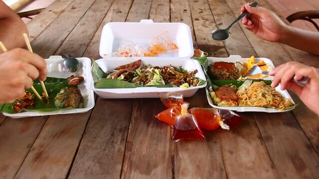Timelapse of two people eating traditional Cambodian dish of Nom Ka Chai or chive cakes, Lort Cha noodles and Kuy Teav Cha  in takeaway packages