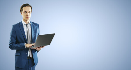 Young businessman in blue suit working with modern laptop, isolated on light blue wall background, with blank place for you text or logo, mockup