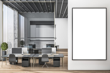 Fototapeta premium Blank white poster in black picture frame on light wall in stylish spacious office area with dark furniture work places, high ceiling, wooden floor and big windows. 3D rendering, mock up